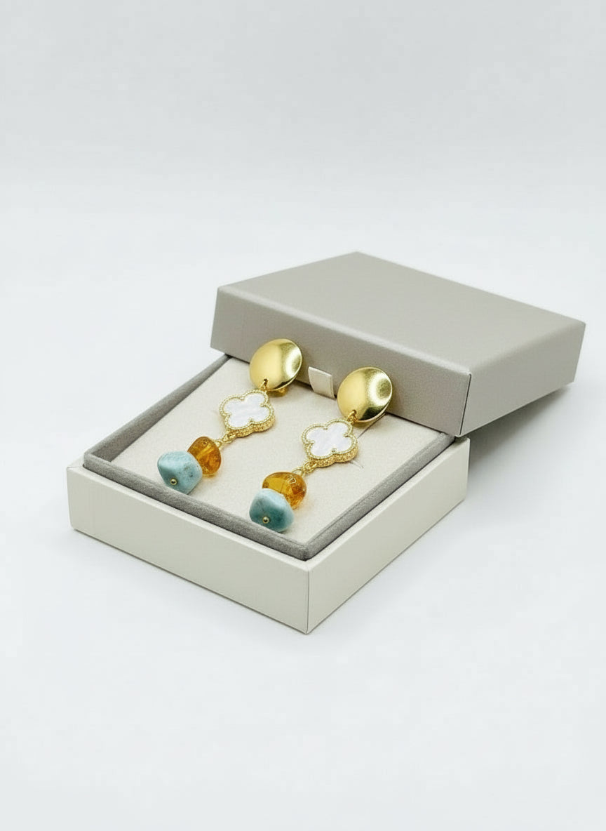 Gold earrings with turquoise and amber beads held in a hand against a light background