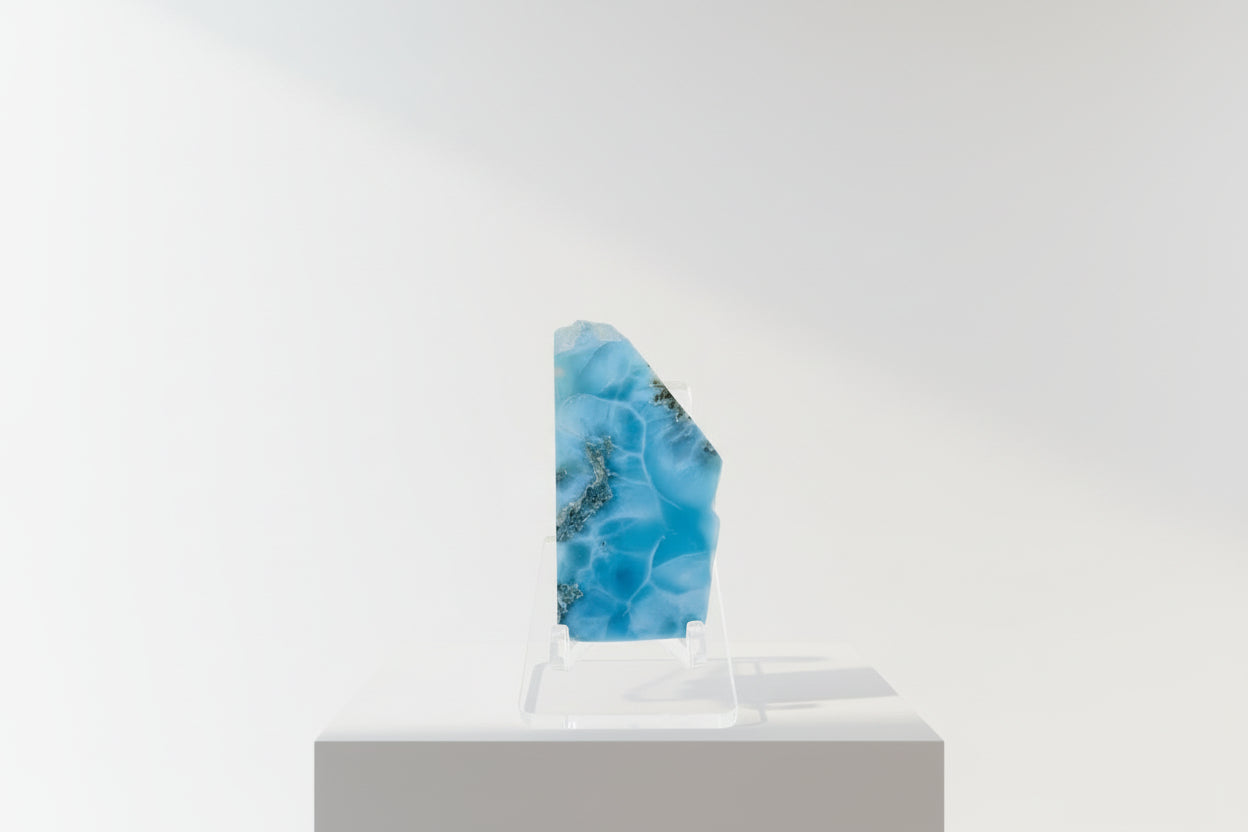 Hand holding a small blue and green marbled stone against a colorful, blurred background