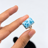 A hand holding a small larimar rectangular ring 