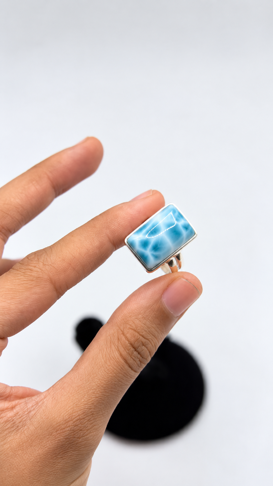 A hand holding a small larimar rectangular ring 