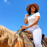 Woman in white outfit and hat riding a horse against a clear blue sky