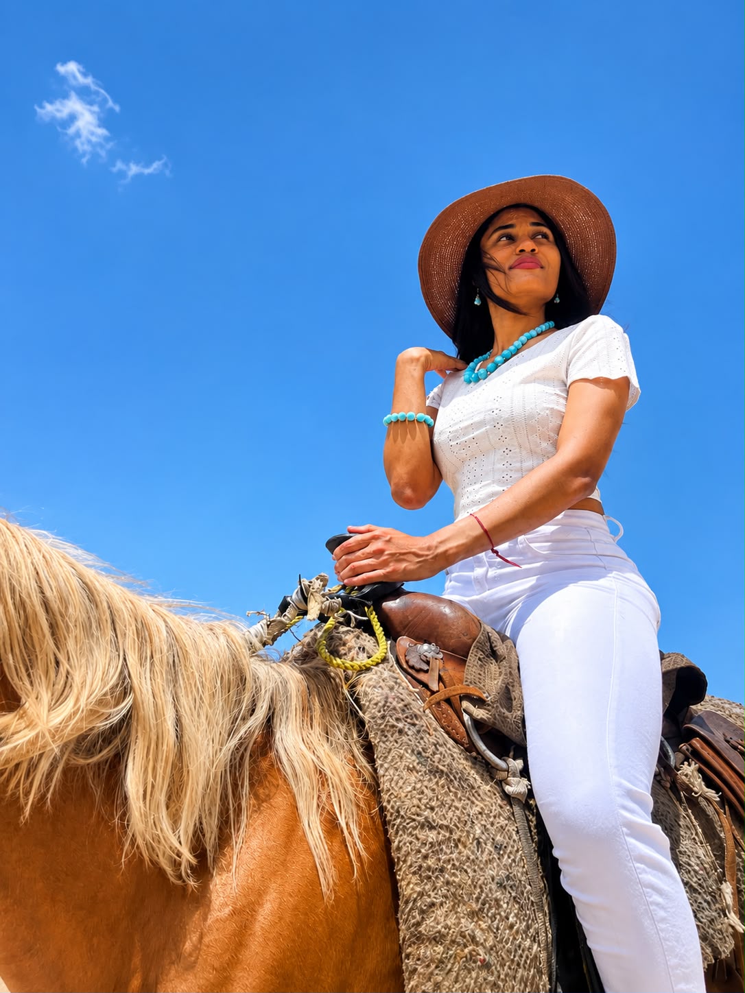 Woman in white outfit and hat riding a horse against a clear blue sky