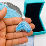 Heart-shaped blue stone pendant held by a hand with turquoise box and card in the background