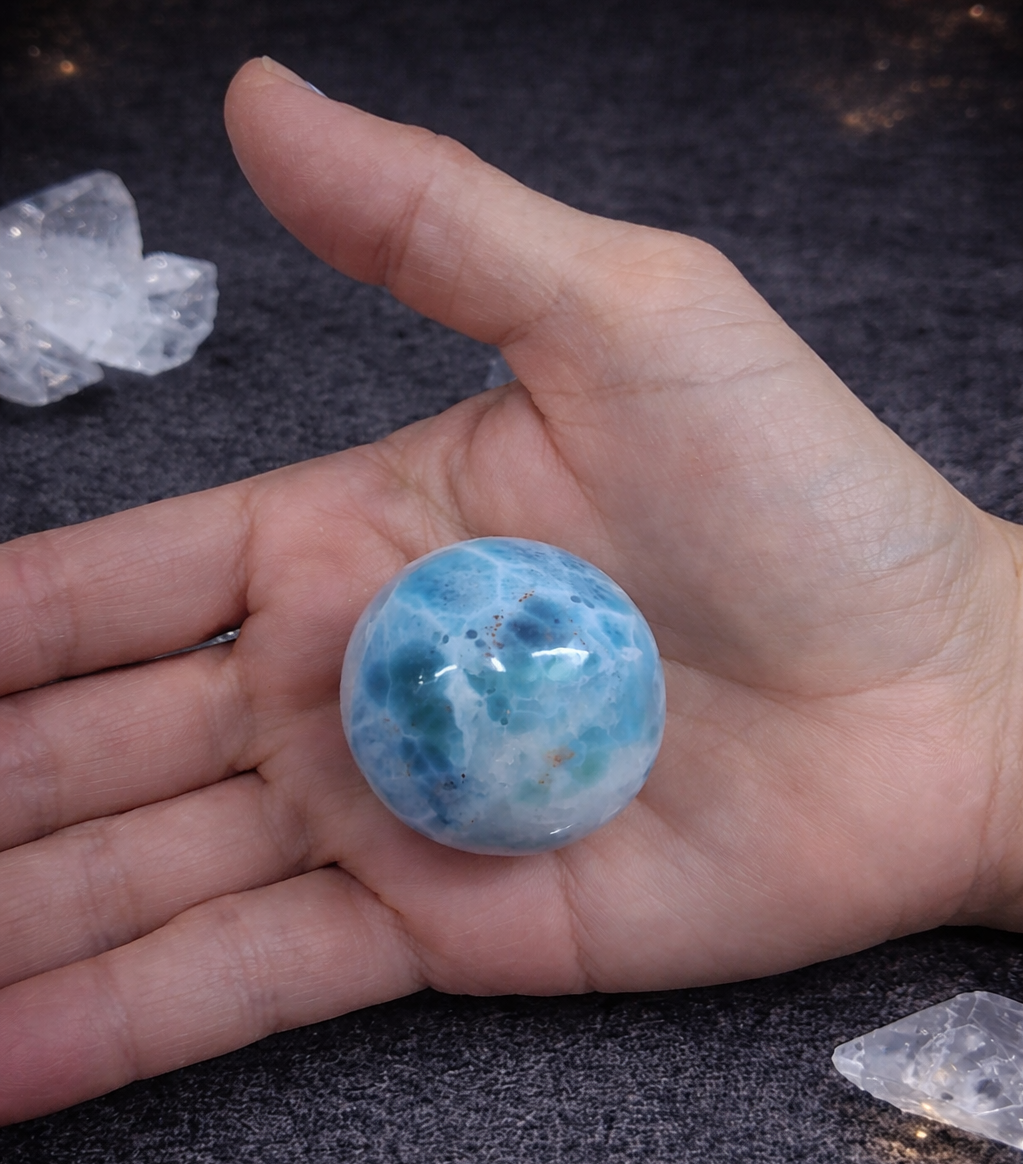 Hand holding a blue crystal ball with crystals on a dark surface