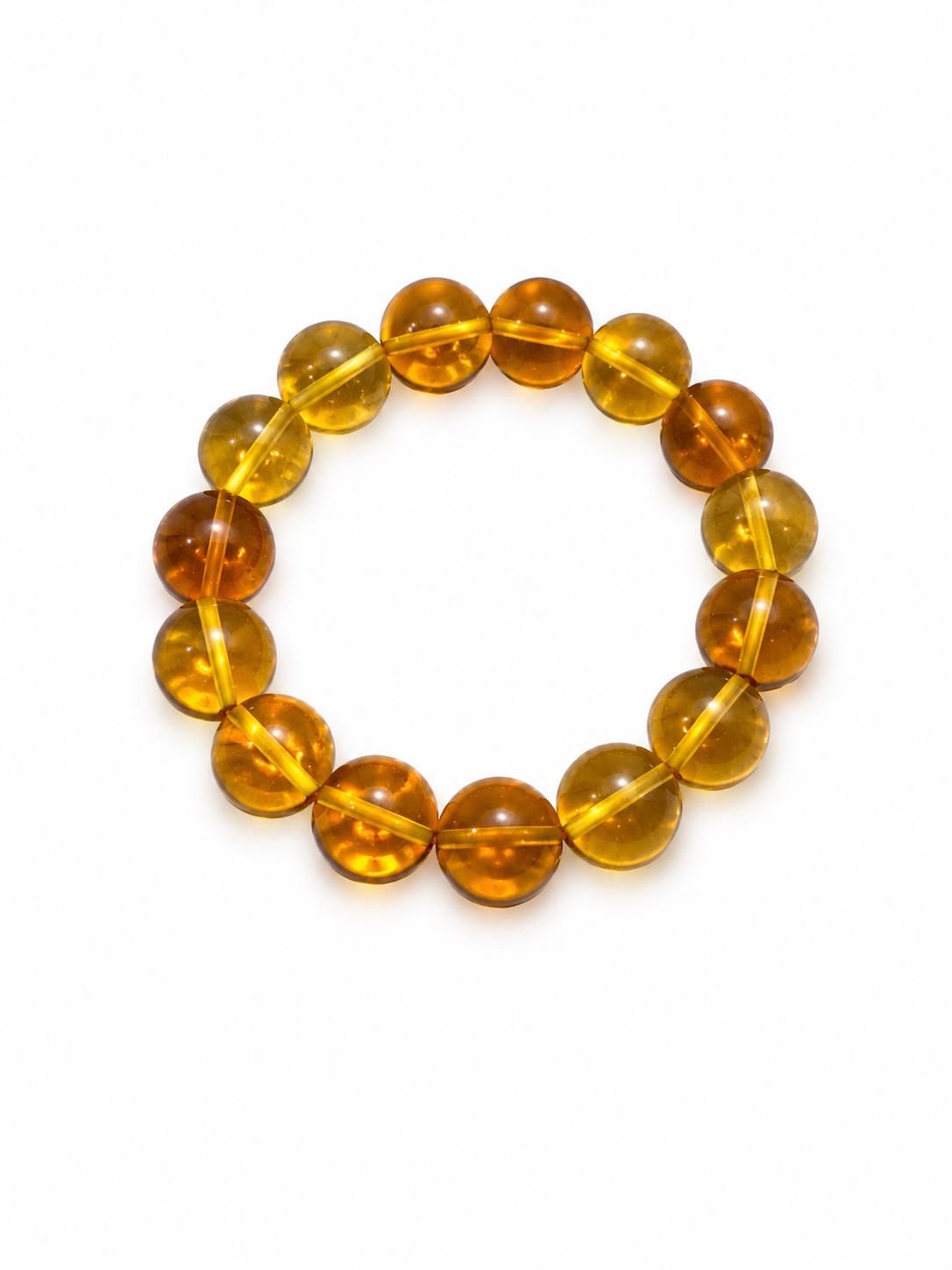 A beaded stretch bracelet made of translucent Dominican
amber beads in warm golden-yellow and orange-brown tones, photographed on a plain white background.