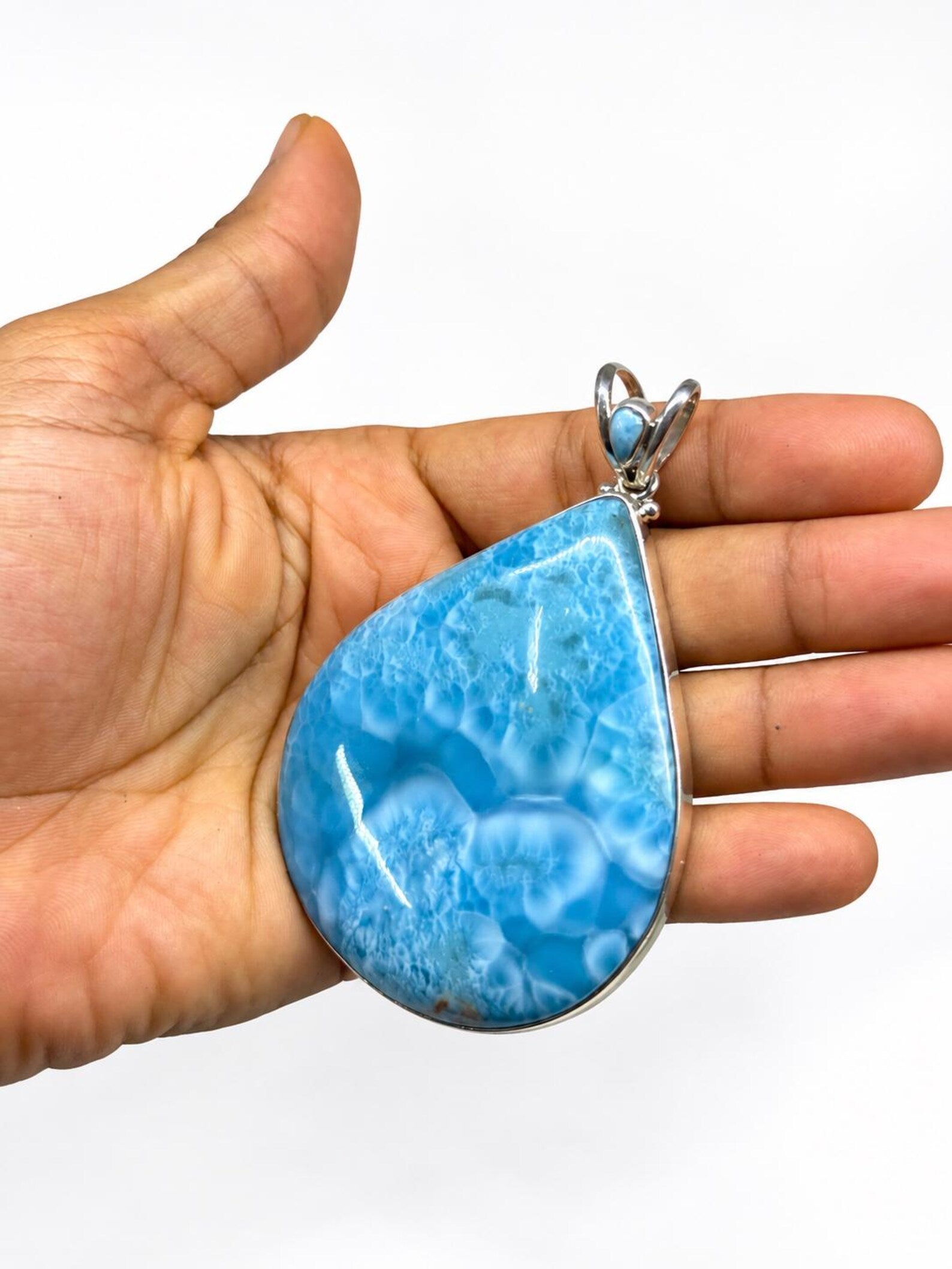 A teardrop-shaped Larimar pendant with a silver bezel setting, held in the palm of a hand against a plain white background.