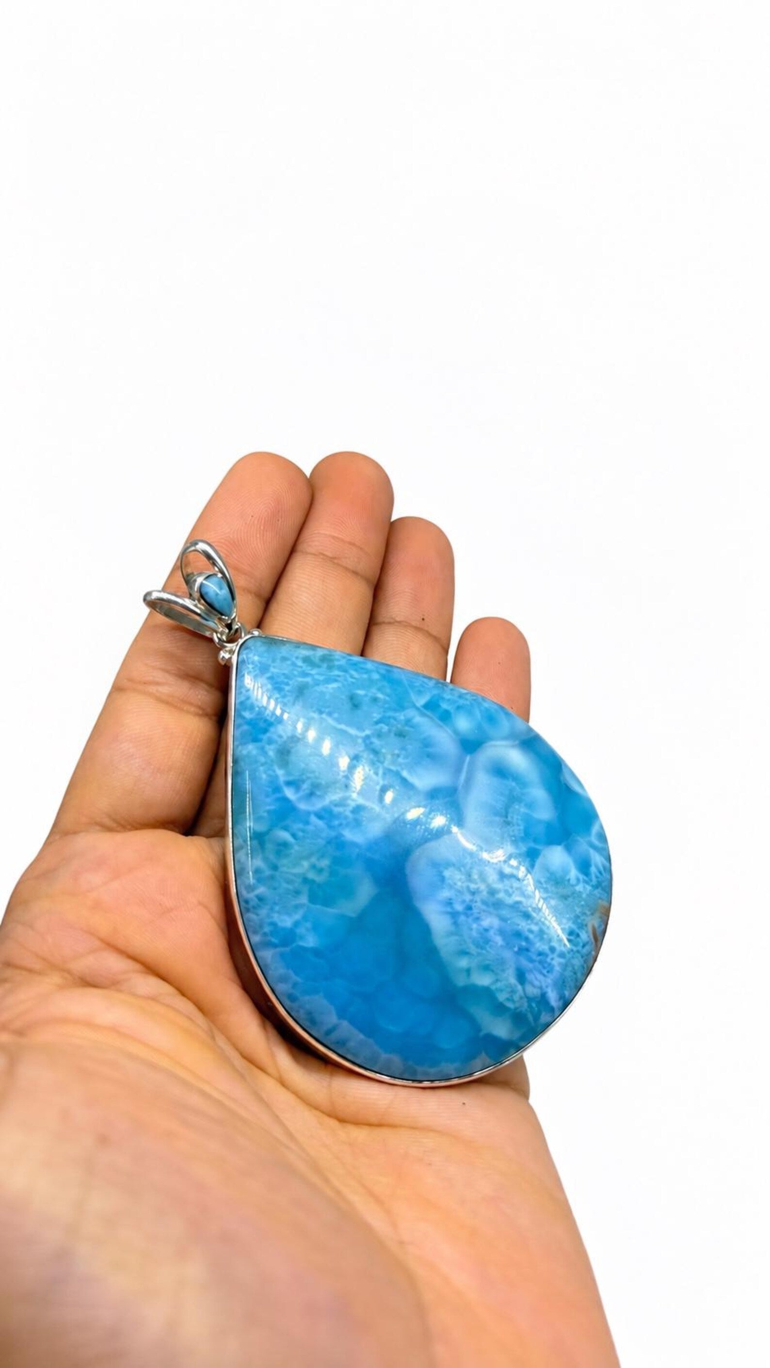 A hand holding a teardrop-shaped blue marbled stone pendant with a silver-toned bezel and bail, shown against a plain white background.