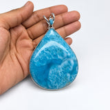 A teardrop-shaped turquoise pendant with a silver bezel setting, held in a person's hand against a plain white background.