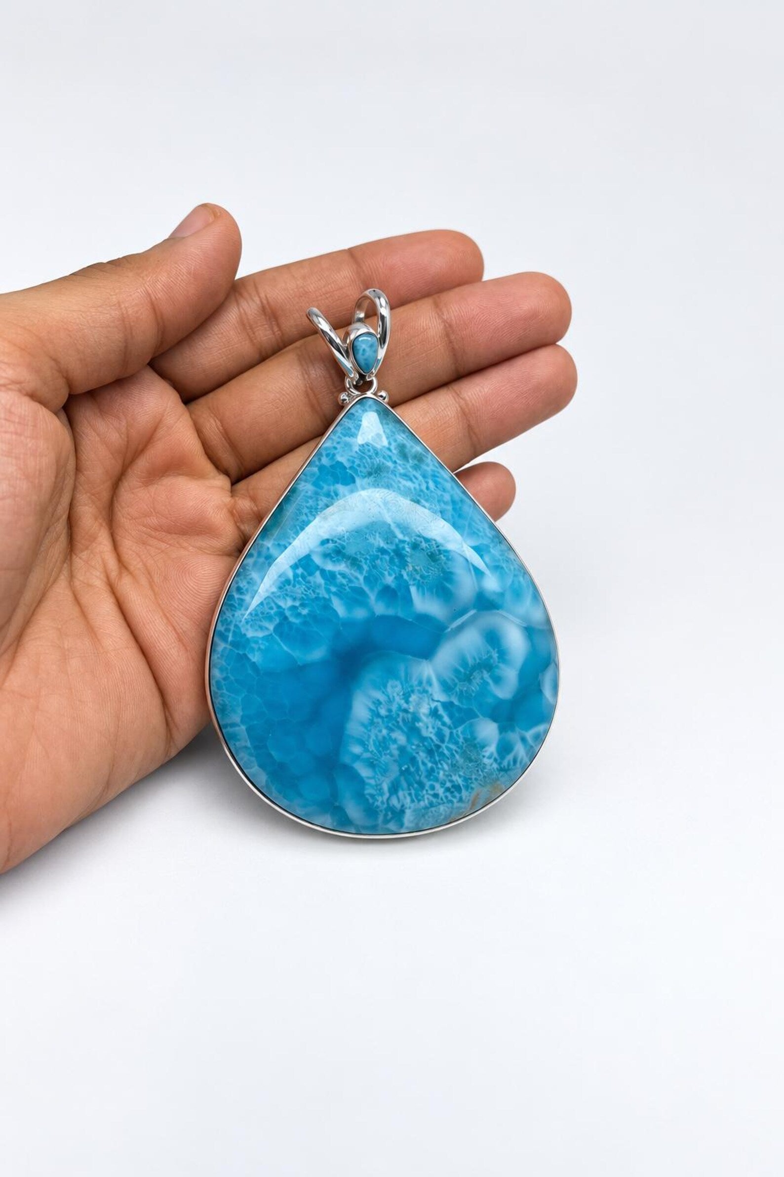 A teardrop-shaped turquoise pendant with a silver bezel setting, held in a person's hand against a plain white background.