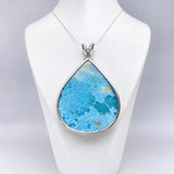 A teardrop-shaped turquoise pendant necklace with a silver bezel and chain, displayed on a white jewelry bust against a light gray background.