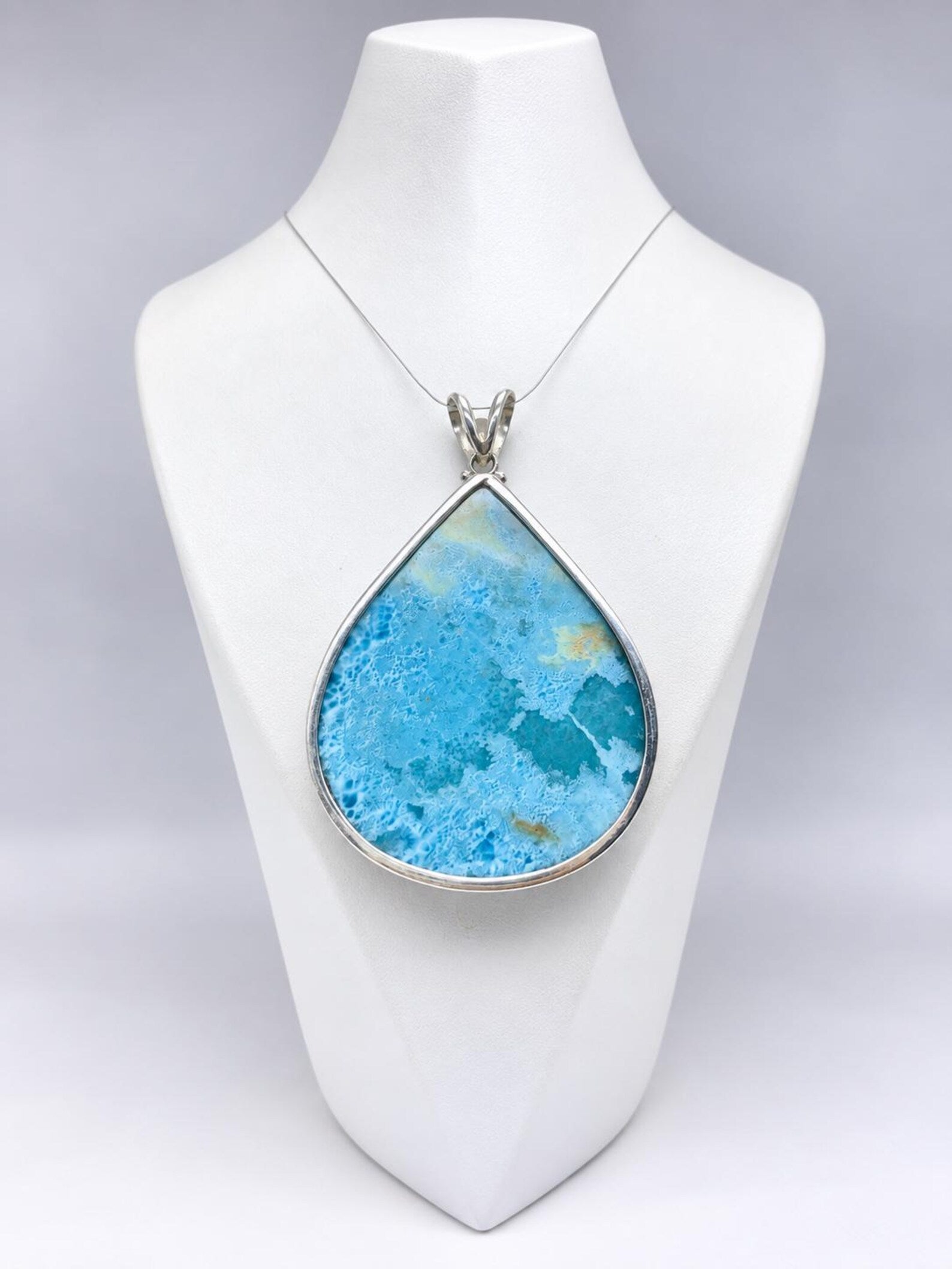 A teardrop-shaped turquoise pendant necklace with a silver bezel and chain, displayed on a white jewelry bust against a light gray background.