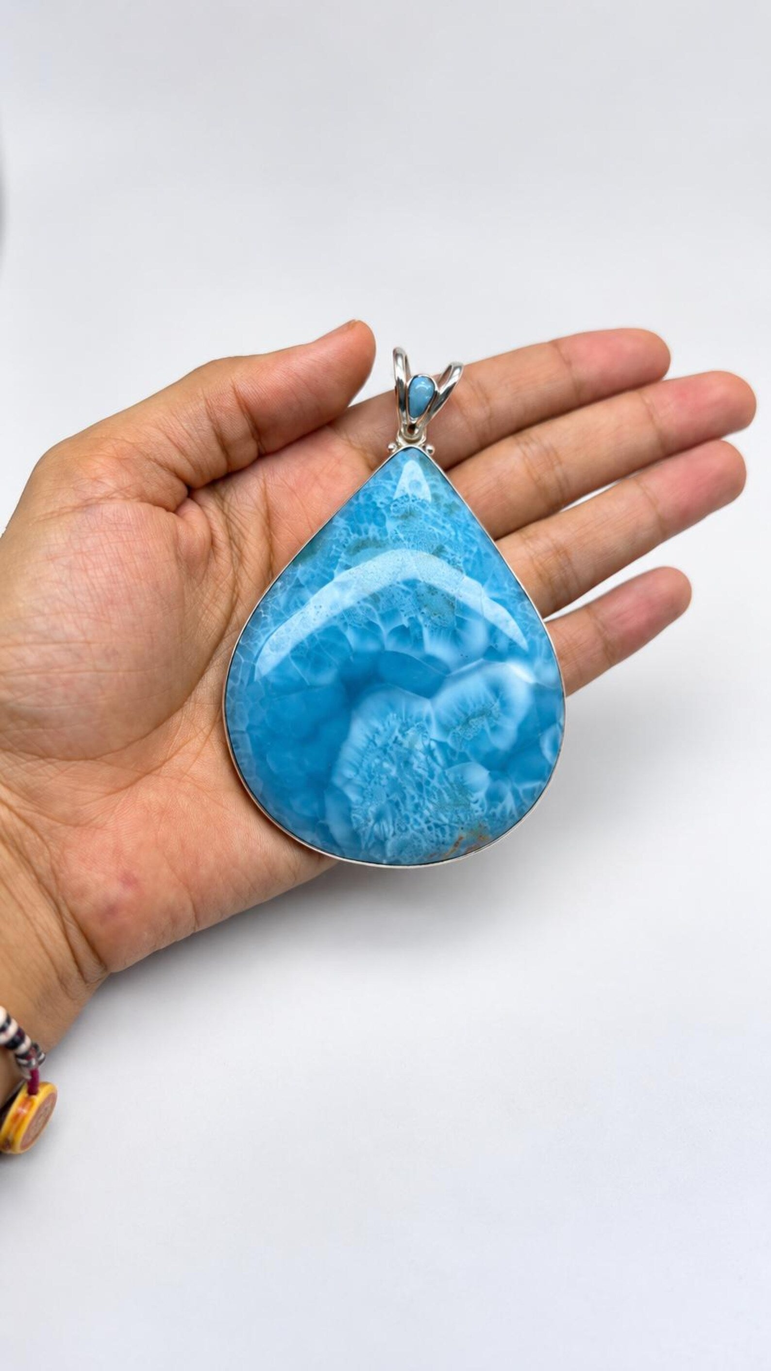 A hand holding a large teardrop-shaped turquoise pendant with a silver-toned setting against a plain white background.