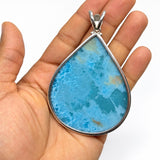 A teardrop-shaped pendant with a vibrant blue marbled stone and a silver bezel setting, held in the palm of a hand against a white background.