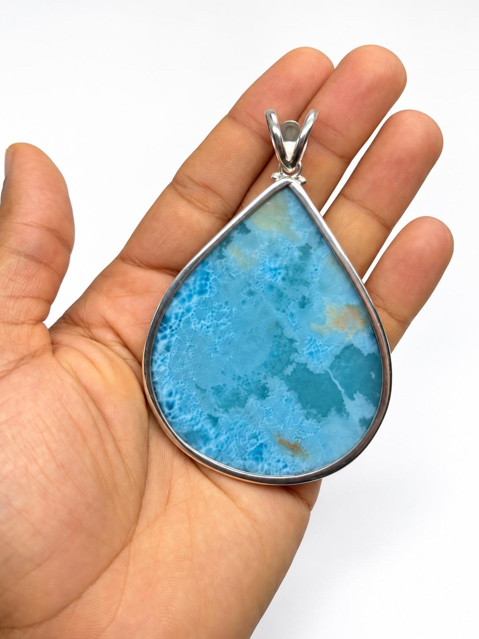 A teardrop-shaped pendant with a vibrant blue marbled stone and a silver bezel setting, held in the palm of a hand against a white background.
