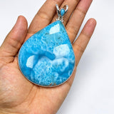 A teardrop-shaped turquoise pendant with a silver bezel setting, held in a person's hand against a plain white background.