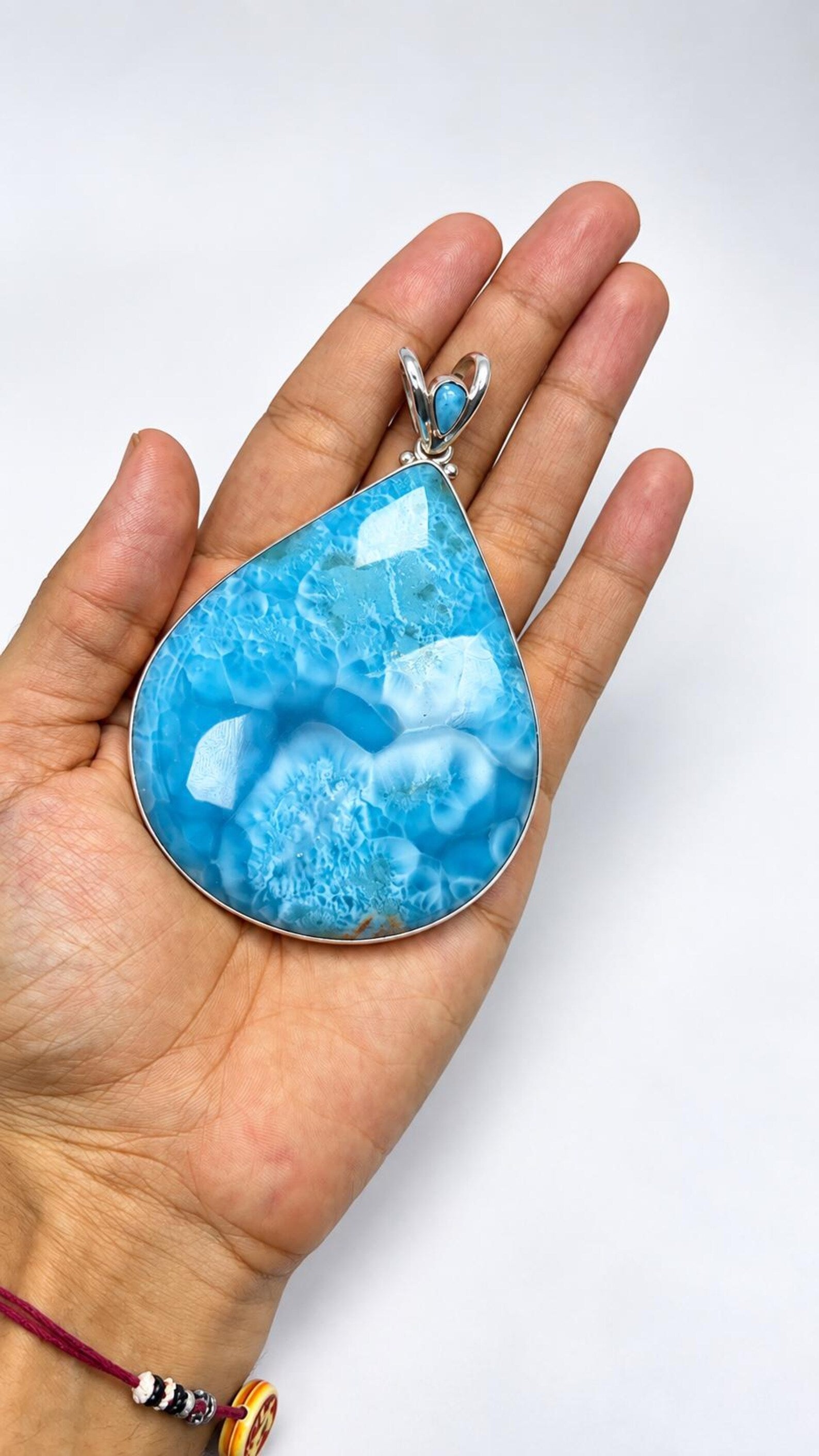 A teardrop-shaped turquoise pendant with a silver bezel setting, held in a person's hand against a plain white background.