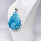 A teardrop-shaped pendant necklace with a vibrant blue marbled stone and a silver bezel setting, displayed on a white mannequin bust against a light gray background.
