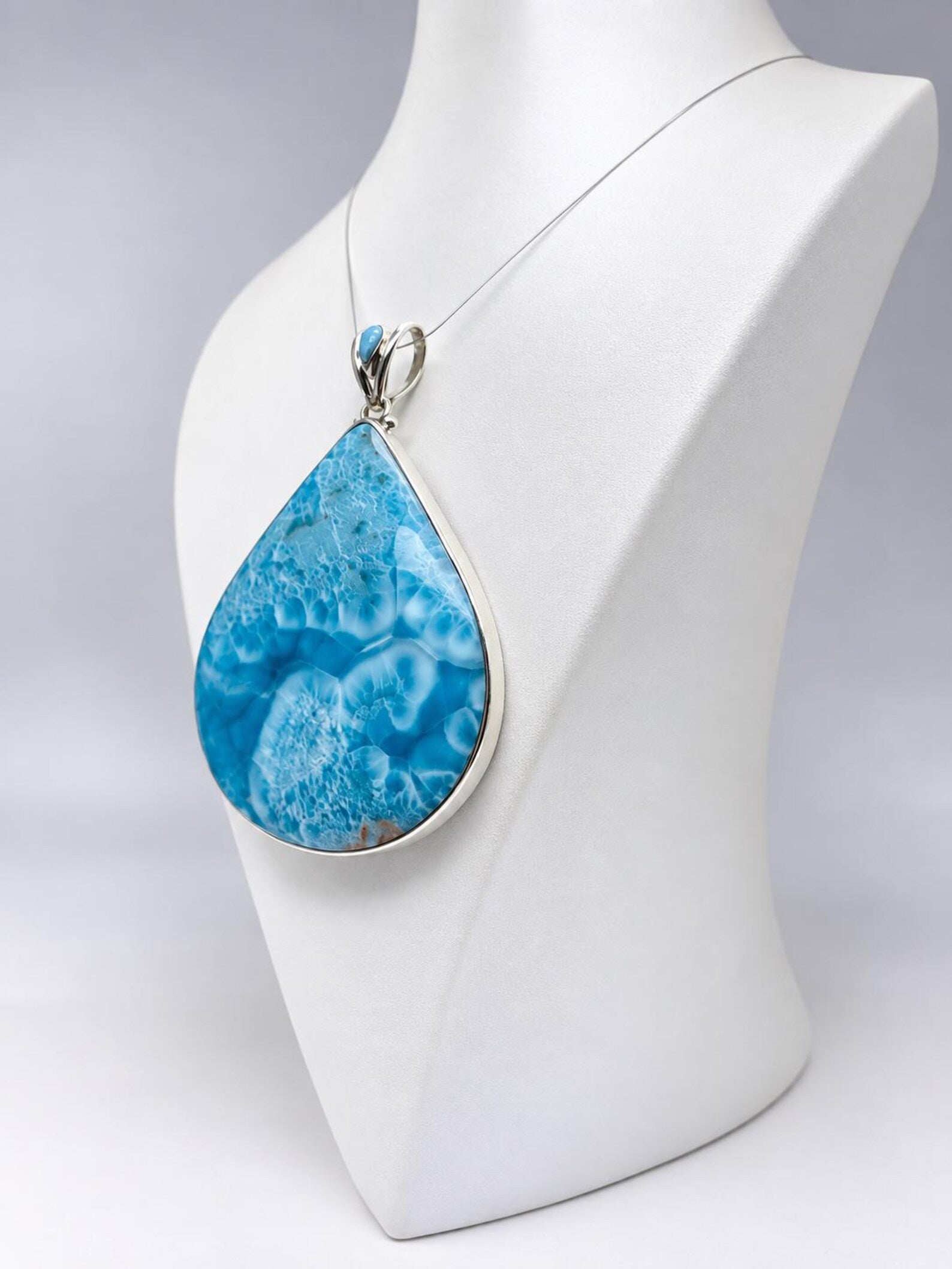 A teardrop-shaped pendant necklace with a vibrant blue marbled stone and a silver bezel setting, displayed on a white mannequin bust against a light gray background.