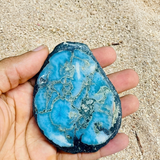 Hand holding a blue and black stone with a textured surface on a sandy background