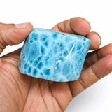 A hand holding a Larimar Stone Freeform, set against a plain white background.