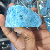 A hand holding a polished blue stone or crystal with natural marbled patterns and a visible crack, photographed against a blurred indoor background.