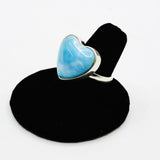 A sterling silver ring featuring a heart-shaped light blue stone, displayed on a black ring stand against a white background.