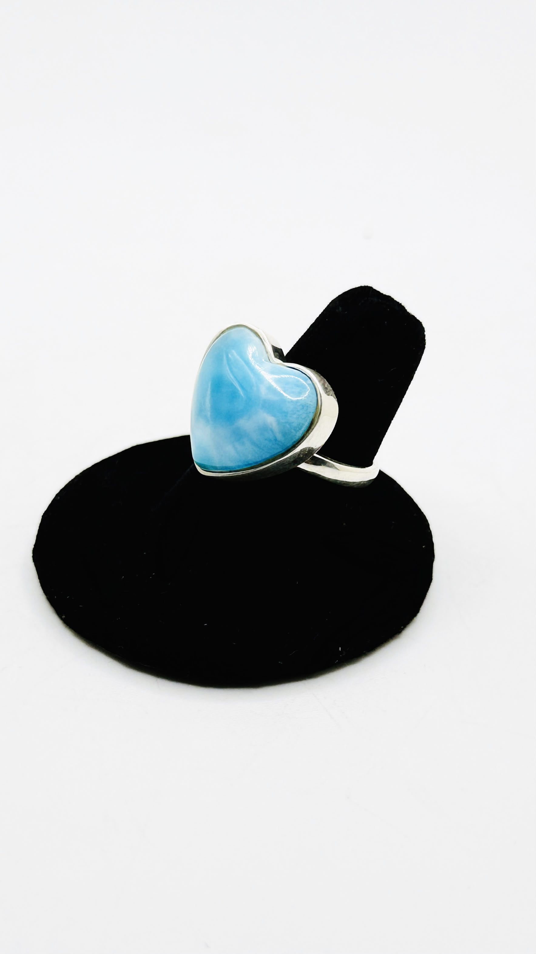 A sterling silver ring featuring a heart-shaped light blue stone, displayed on a black ring stand against a white background.