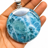 AAA Larimar round cabochon pendant in hand – deep ocean-blue with white fractal starburst pattern – genuine Dominican Republic gemstone