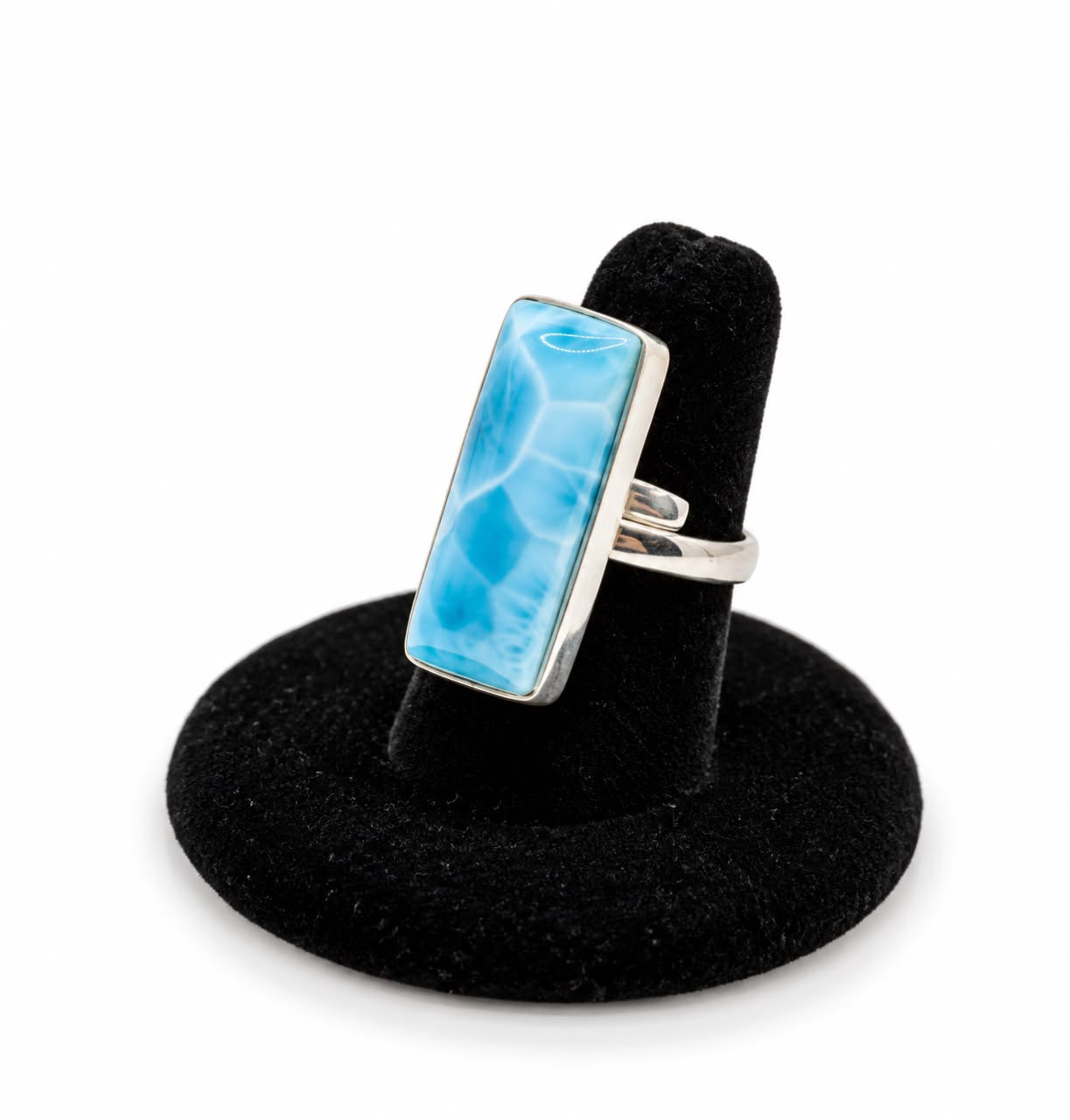 A silver larimar  ring with a rectangular light blue marbled stone, displayed on a black velvet ring stand against a white background.