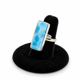 A silver larimar  ring with a rectangular light blue marbled stone, displayed on a black velvet ring stand against a white background.