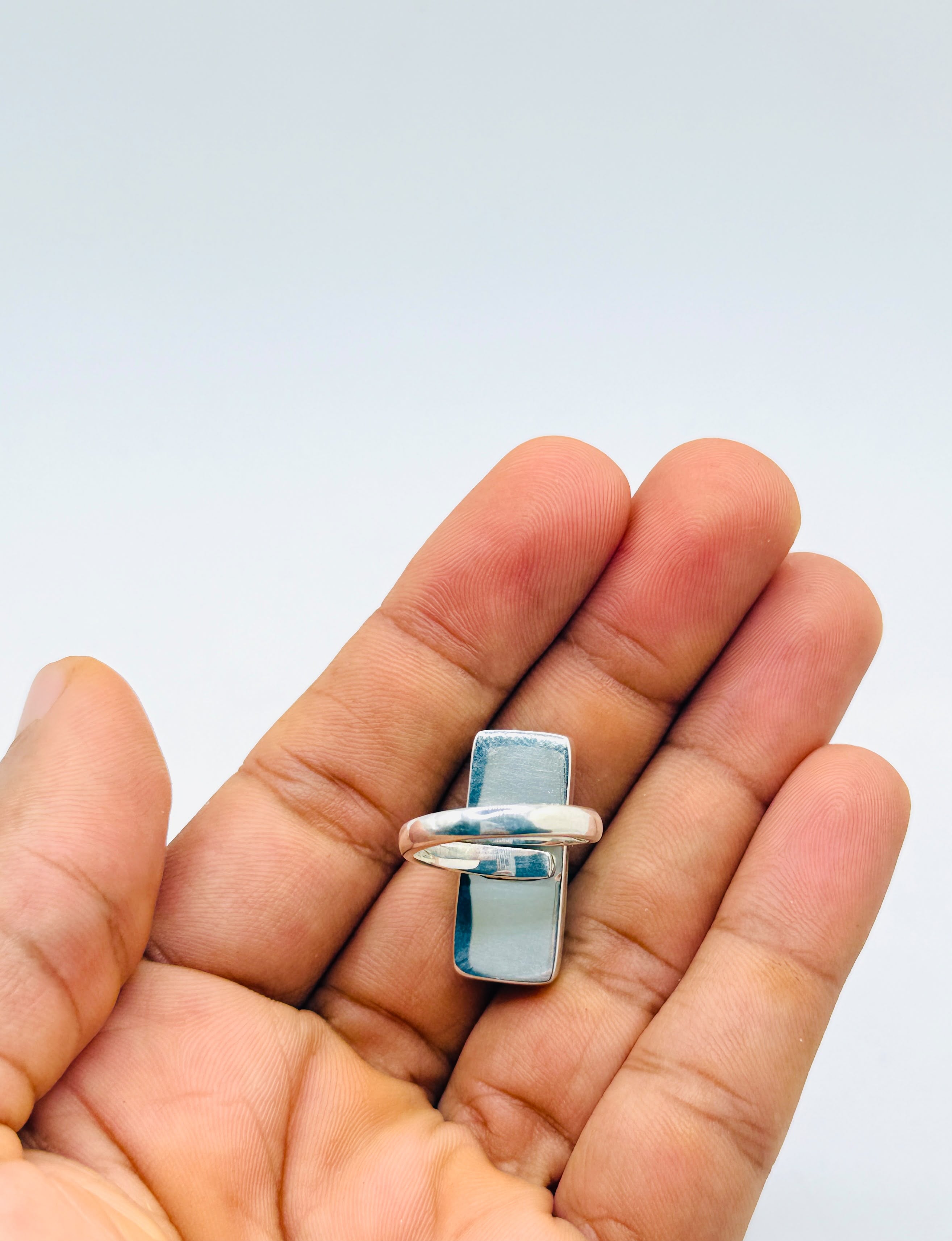 A silver ring with a rectangular light blue stone, held on the fingers of a hand against a plain light gray background.
