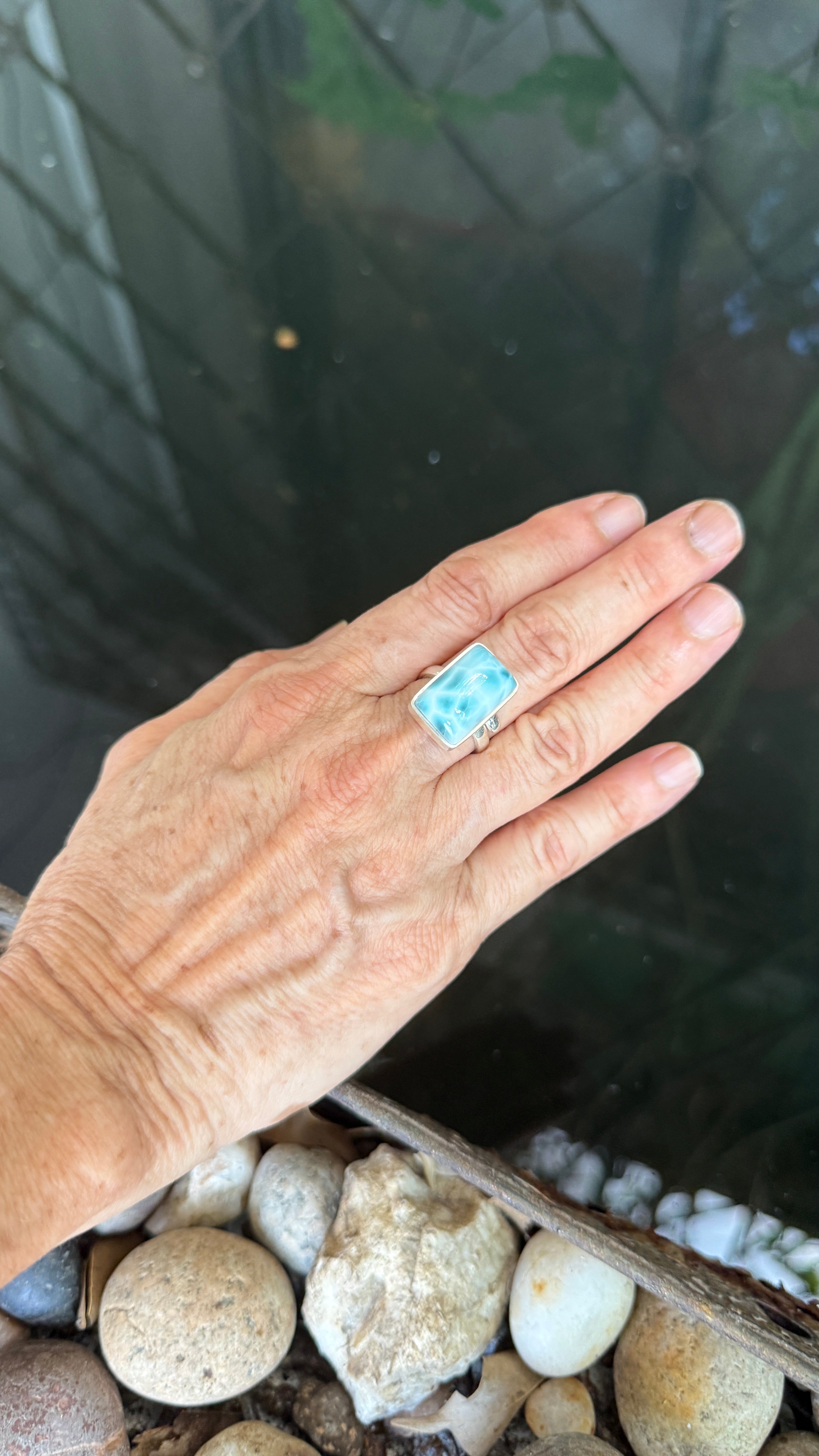 A hand wearing a silver ring with a rectangular larimar stone.