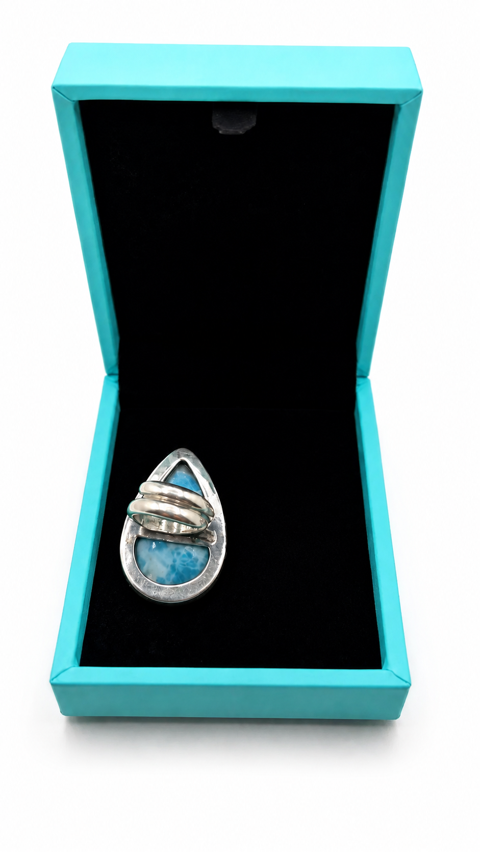 A silver ring with a teardrop-shaped blue stone inlay, displayed inside an open turquoise jewelry box with a black velvet lining on a white background.