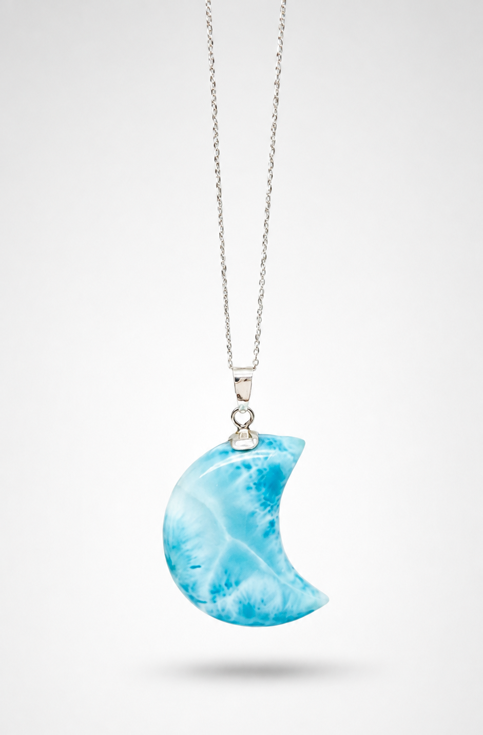 A silver necklace with a crescent moon pendant made of marbled blue and white stone, shown against a light gray background.