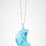 A silver necklace with a crescent moon pendant made of marbled blue and white stone, shown against a light gray background.