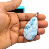 A hand holds a larimar stone teardrop-shaped pendant 