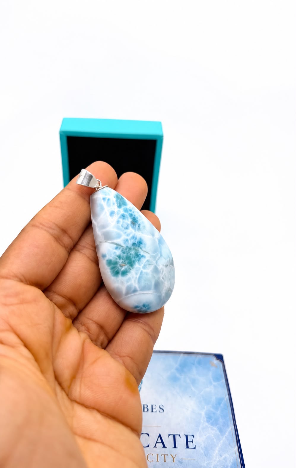 A hand holds a teardrop-shaped Larimar stone pendant 