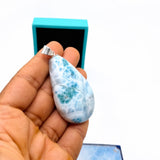 A hand holds a teardrop-shaped Larimar stone pendant 
