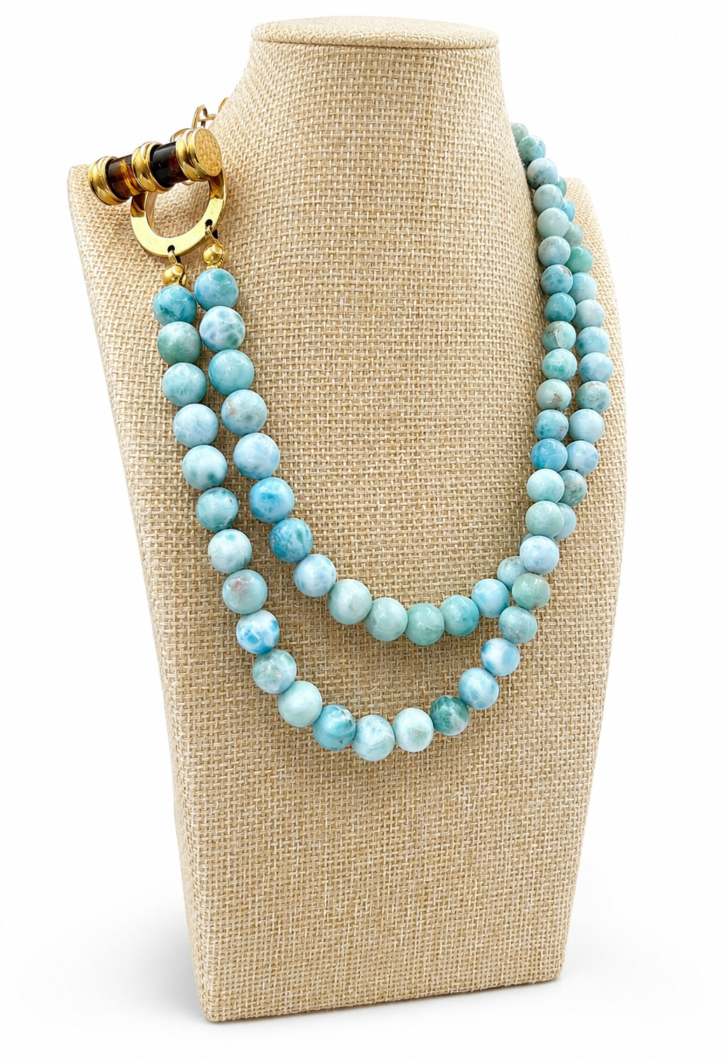 A double-strand beaded necklace with light blue marbled beads and a gold-toned clasp, displayed on a beige fabric jewelry bust against a white background.