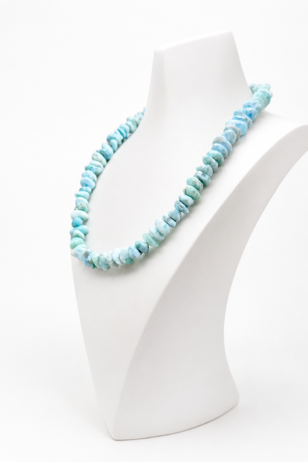 A Larimar bead
 necklace made of small irregular shell-like pieces in light blue and aqua tones, displayed on a white jewelry bust against a clean white background.