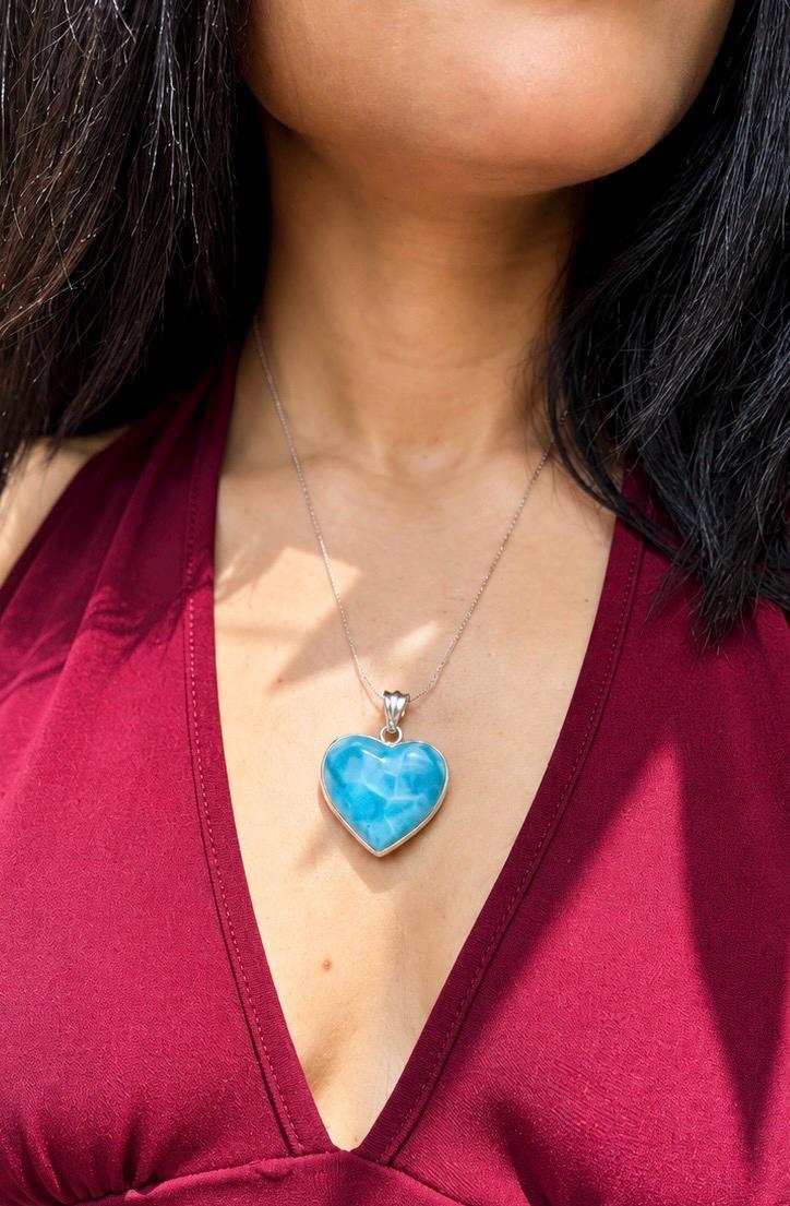 A close-up of a person wearing a silver heart-shaped pendant necklace with a vibrant blue marbled stone, styled with a deep burgundy V-neck top.
