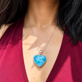 A close-up of a person wearing a silver heart-shaped pendant necklace with a vibrant blue marbled stone, styled with a deep burgundy V-neck top.