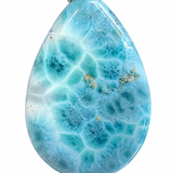 A teardrop-shaped Larimar pendant featuring a vibrant light blue and white marbled pattern with small gold inclusions, suspended from a silver bail, set against a plain white background.