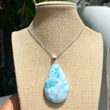 A teardrop-shaped Larimar pendant necklace with a light blue and white.