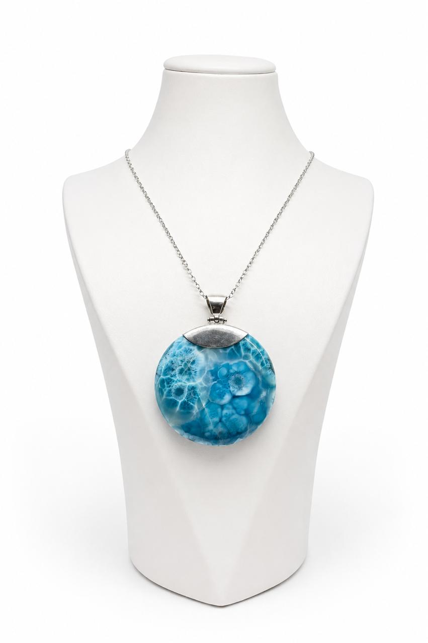 A silver chain larimar necklace with a round pendant featuring a textured blue and white pattern, displayed on a white mannequin bust against a white background.