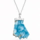 A silver necklace featuring a polished bluelarimar  crystal pendant with natural inclusions, suspended from a delicate silver chain against a white background.