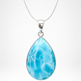 A Larimar teardrop-shaped pendant necklace featuring a vibrant blue marbled stone with white veining, suspended from a delicate silver chain against a light gray background.