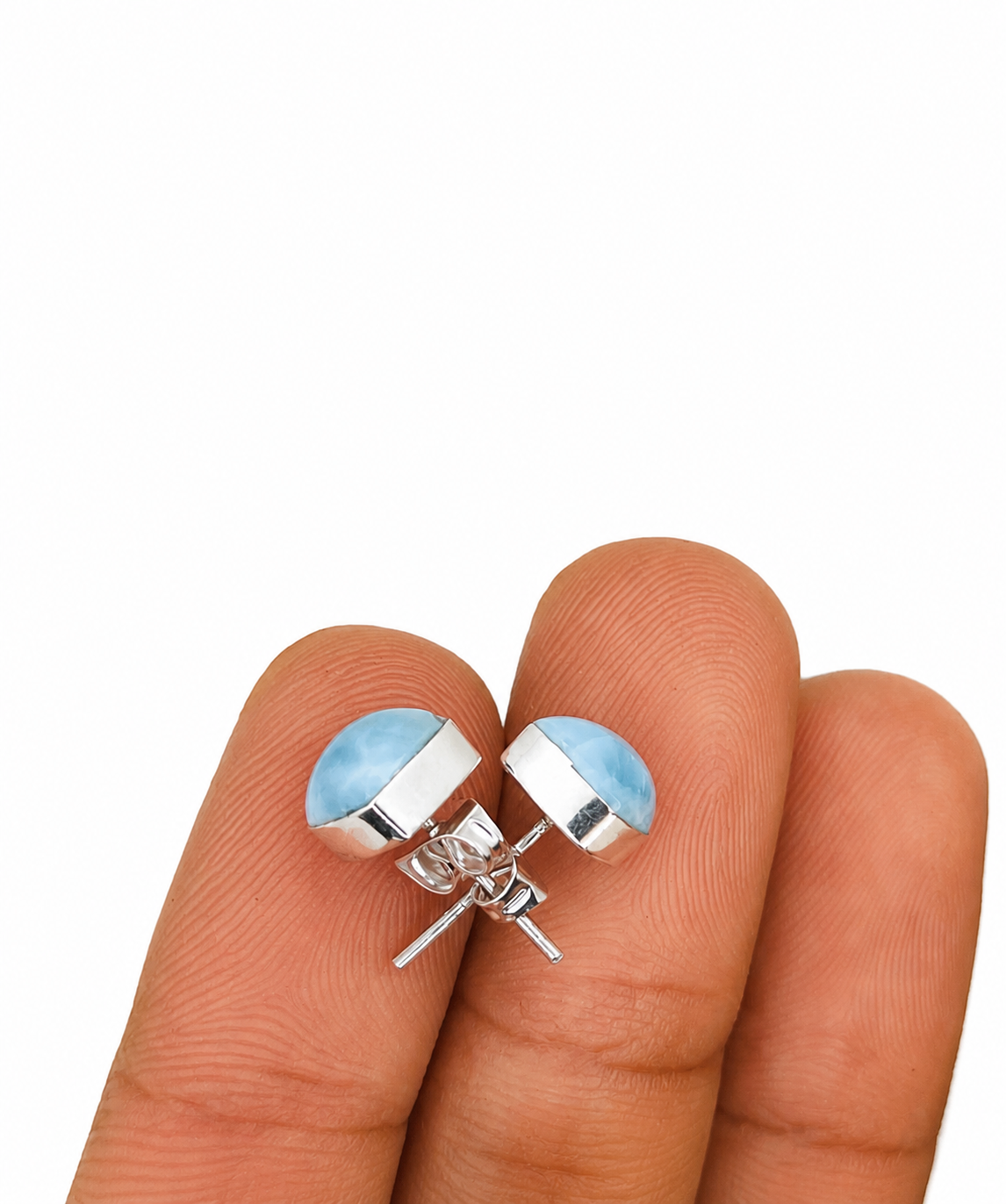 A pair of silver stud earrings with light blue oval inlays, shown resting on a person's fingers against a plain white background.