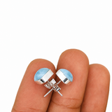 A pair of silver stud earrings with light blue oval inlays, shown resting on a person's fingers against a plain white background.