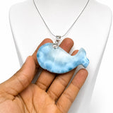 A light blue and white marbled whale-shaped pendant necklace held in a hand in front of a white mannequin bust.